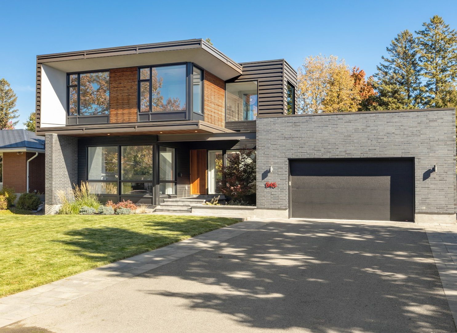 Modernes zweigeschossiges Haus mit Holz- und Steinverkleidung, Garage und Garten.
