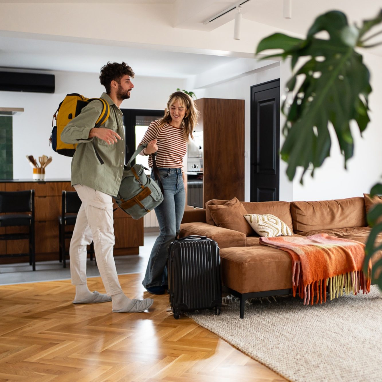 Junges Paar mit Reisegepäck betritt ein stilvolles Wohnzimmer.