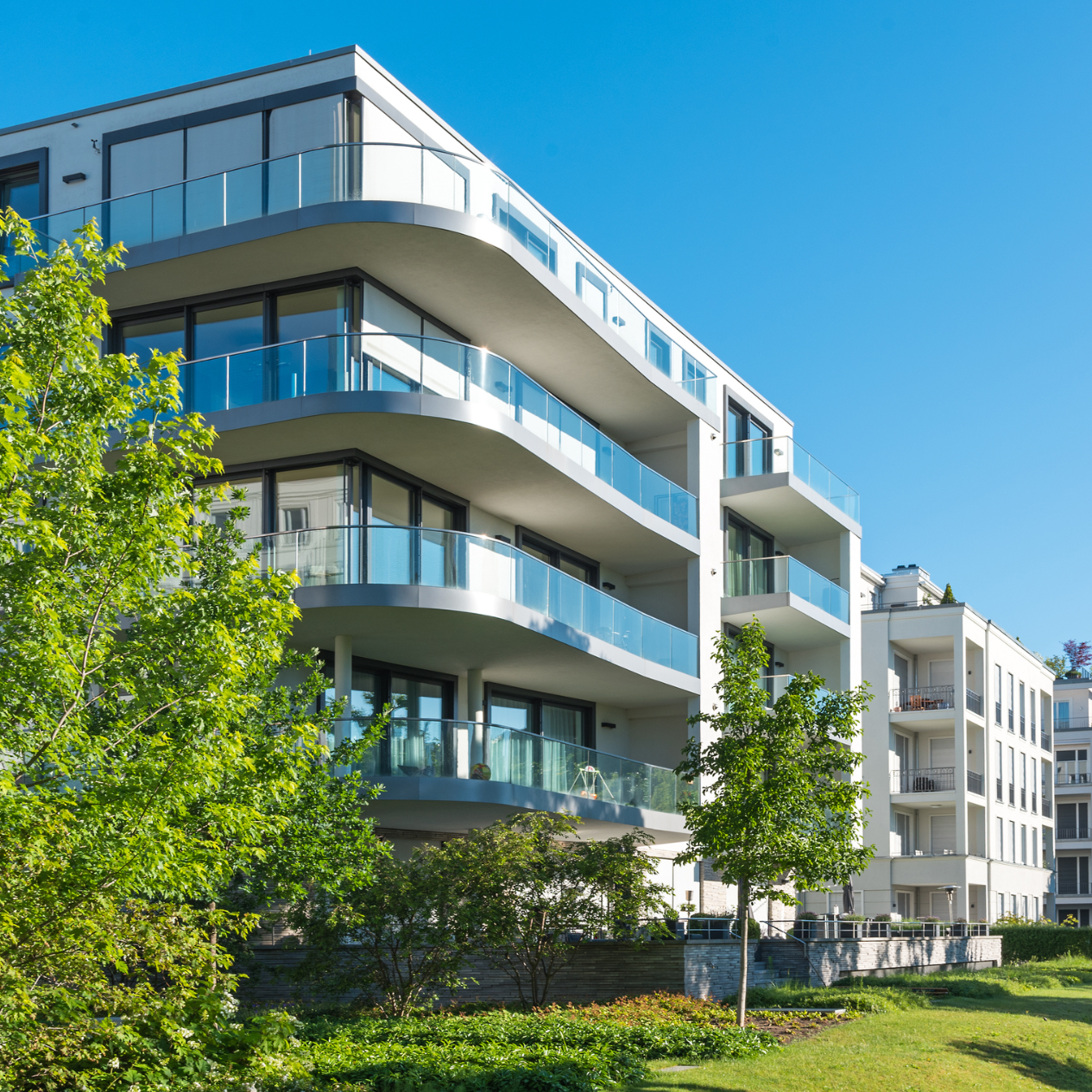 Moderne Wohnanlage mit Balkonen, umgeben von Bäumen und klarem, blauem Himmel.