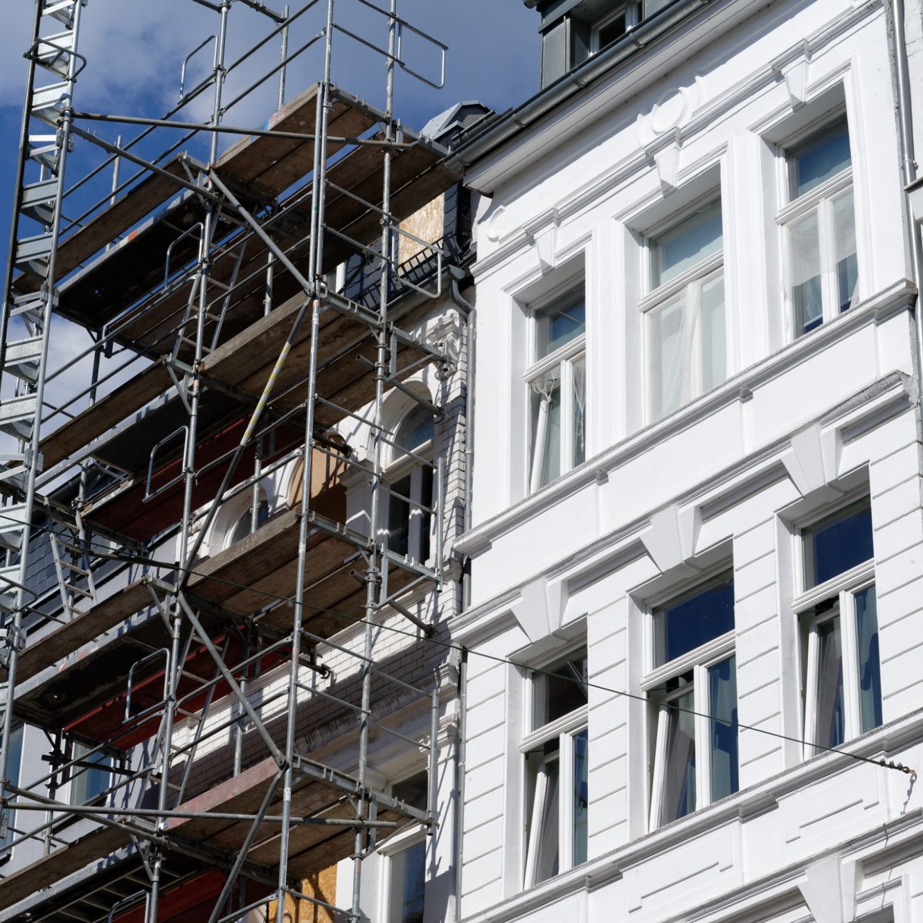 Baugerüst an einer weißen Wohngebäudefassade mit Fenstern.