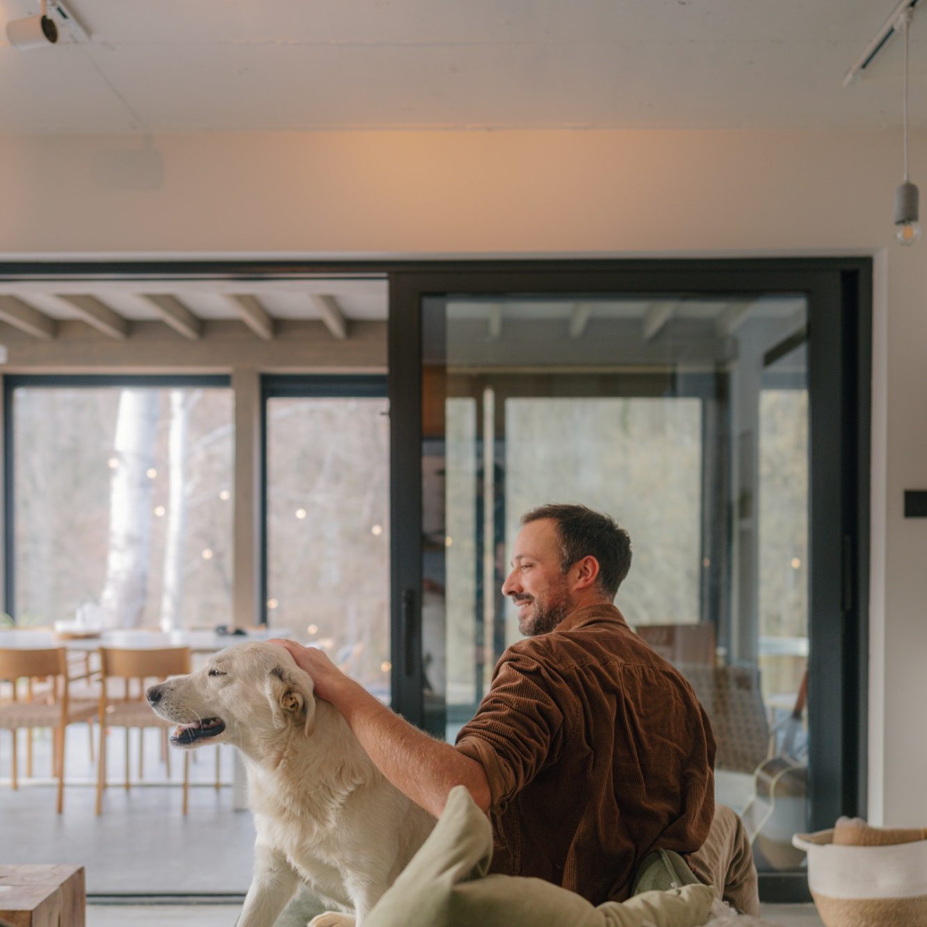 Mann sitzt auf einer Couch und streichelt einen Hund in einem modernen Raum.